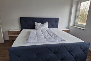A bedroom with a large bed, a dark headboard, a window, and a bedside table. - Holiday home in Minsen with swimming pool (Minsen)