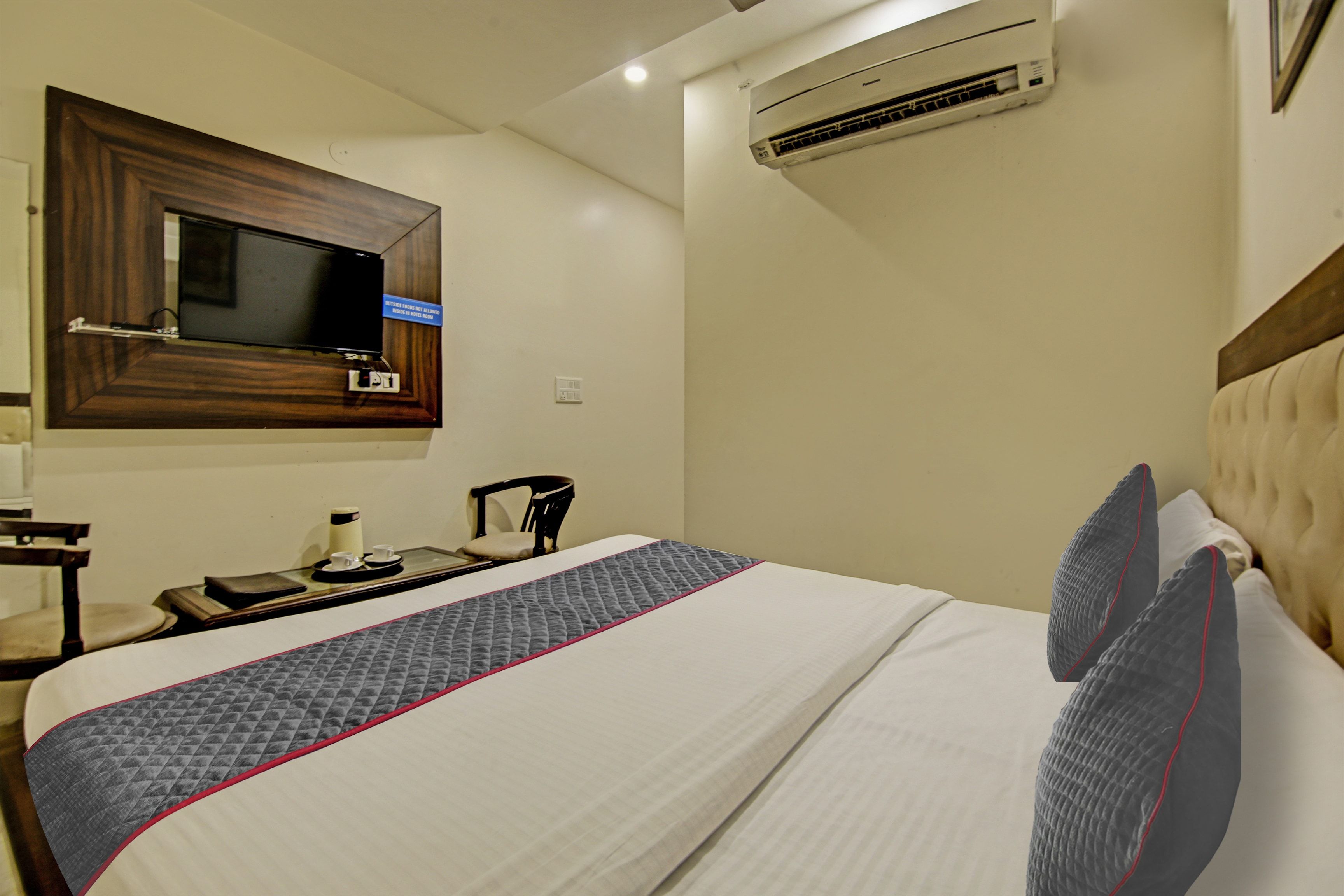 A hotel room with a bed, a television mounted on the wall, and an air conditioning unit.