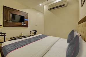 A hotel room with a bed, a television mounted on the wall, and an air conditioning unit. - Townhouse Grand Inn (Ghaziabad)
