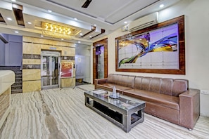 A lobby with a marble floor, a brown leather sofa, a glass coffee table, and a large abstract painting. - Townhouse Grand Inn (Ghaziabad)