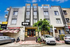 Un hotel con fachada moderna, un cartel que dice 'OYO HOTEL GRAND' y una entrada visible con escalones que conducen a la puerta.