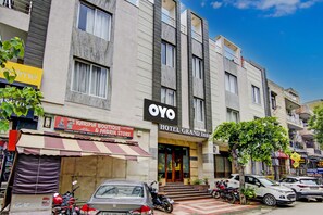 Un hotel con fachada moderna, entrada visible y cartel de una tienda de modas y telas.