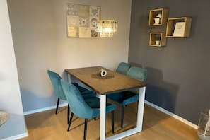 A dining area with a wooden table, teal chairs, and a chandelier. - House at the dike 12c (Varel\/Dangast)