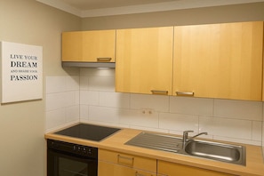 A kitchen with wooden cabinets, a black stove, a sink, and a backsplash. - House at the dike 12c (Varel\/Dangast)