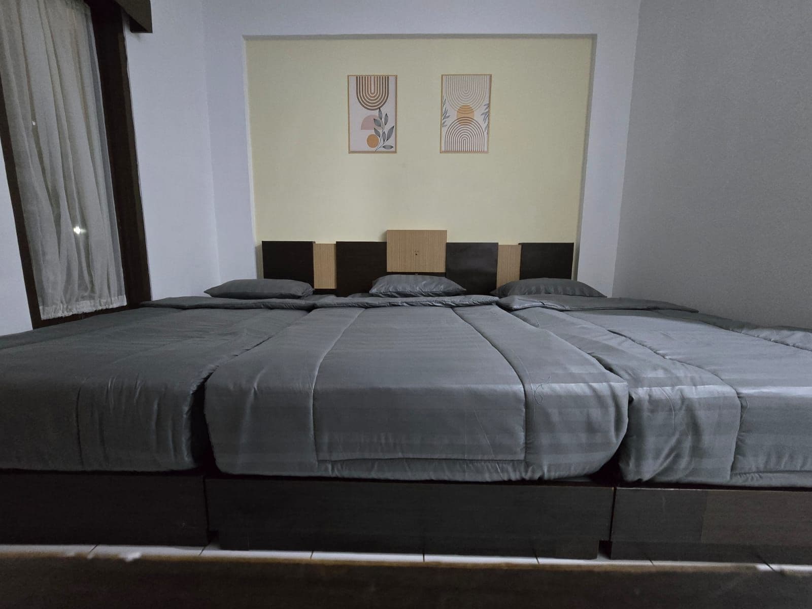 Un lit avec une tête de lit, une literie grise et deux œuvres d’art accrochées au mur.