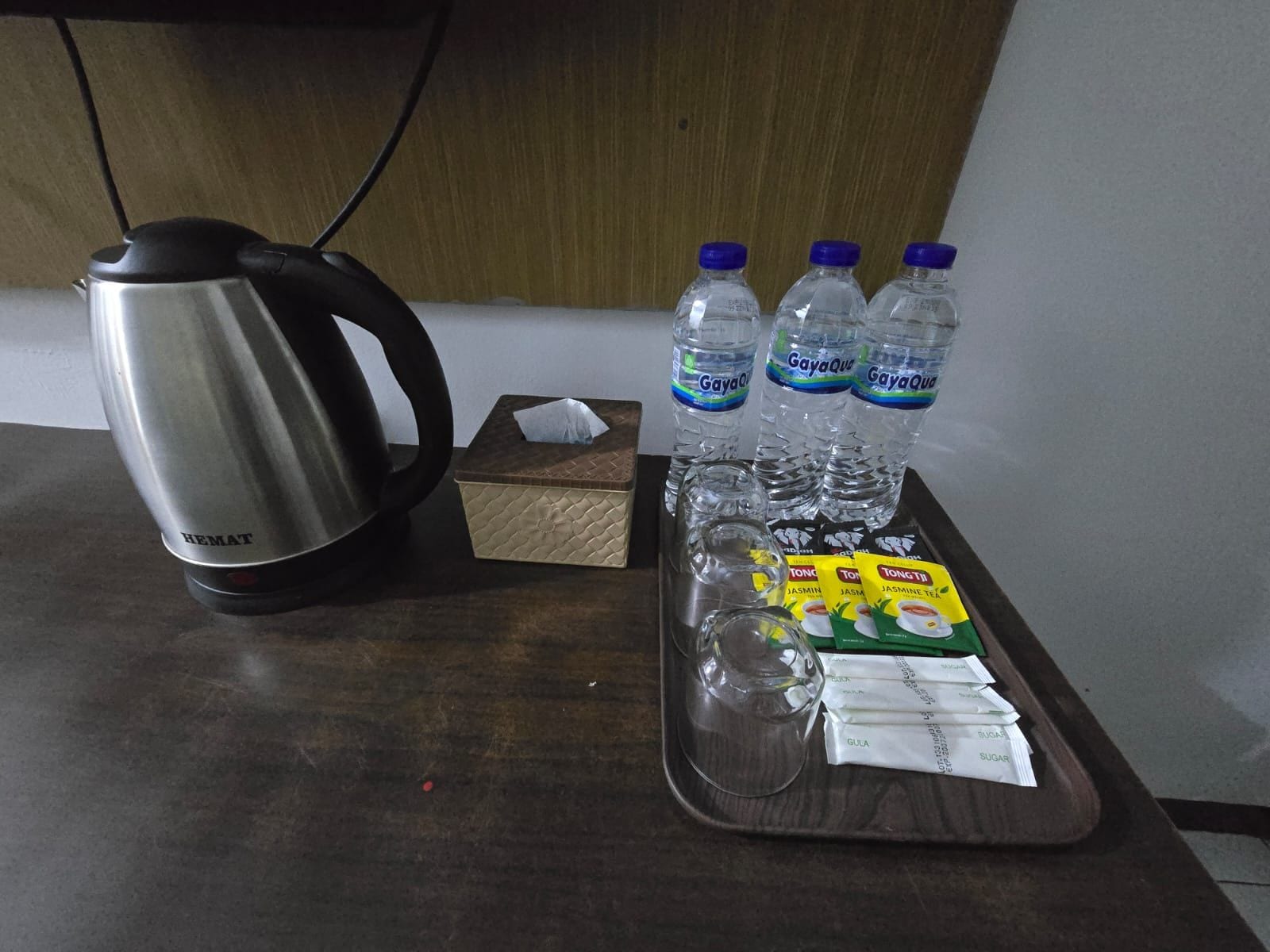Una encimera de cocina con un hervidor, botellas de agua, una caja de pañuelos y sobres de té.