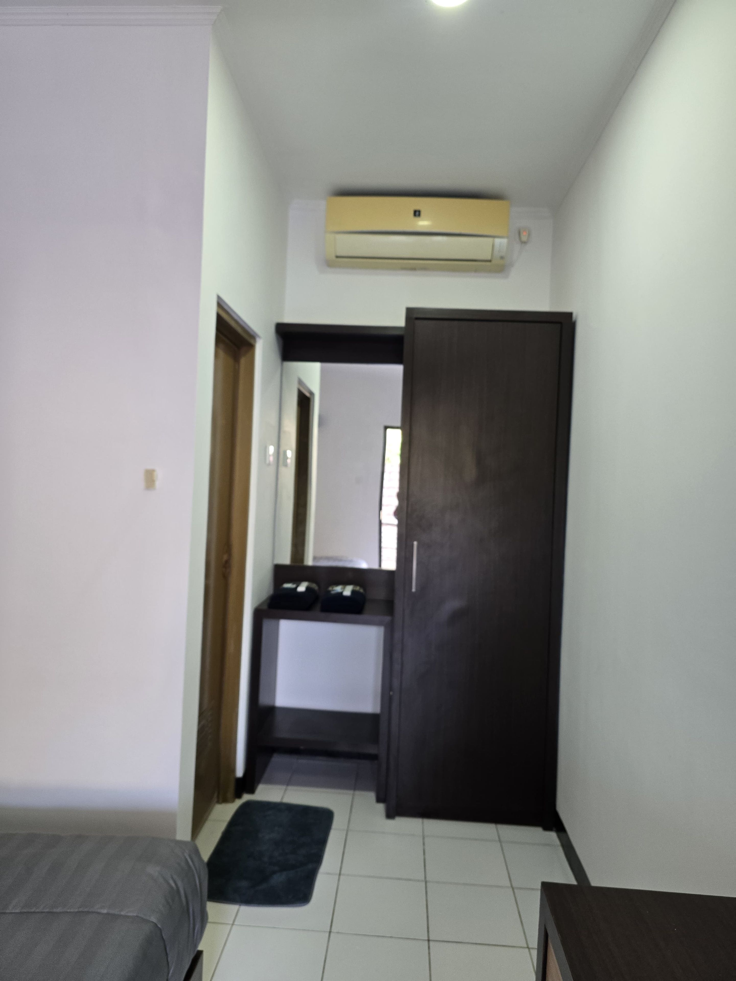 Una habitación pequeña con cama, un escritorio, un armario y un equipo de aire acondicionado.