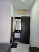 Una habitación pequeña con cama, un escritorio, un armario y un equipo de aire acondicionado.