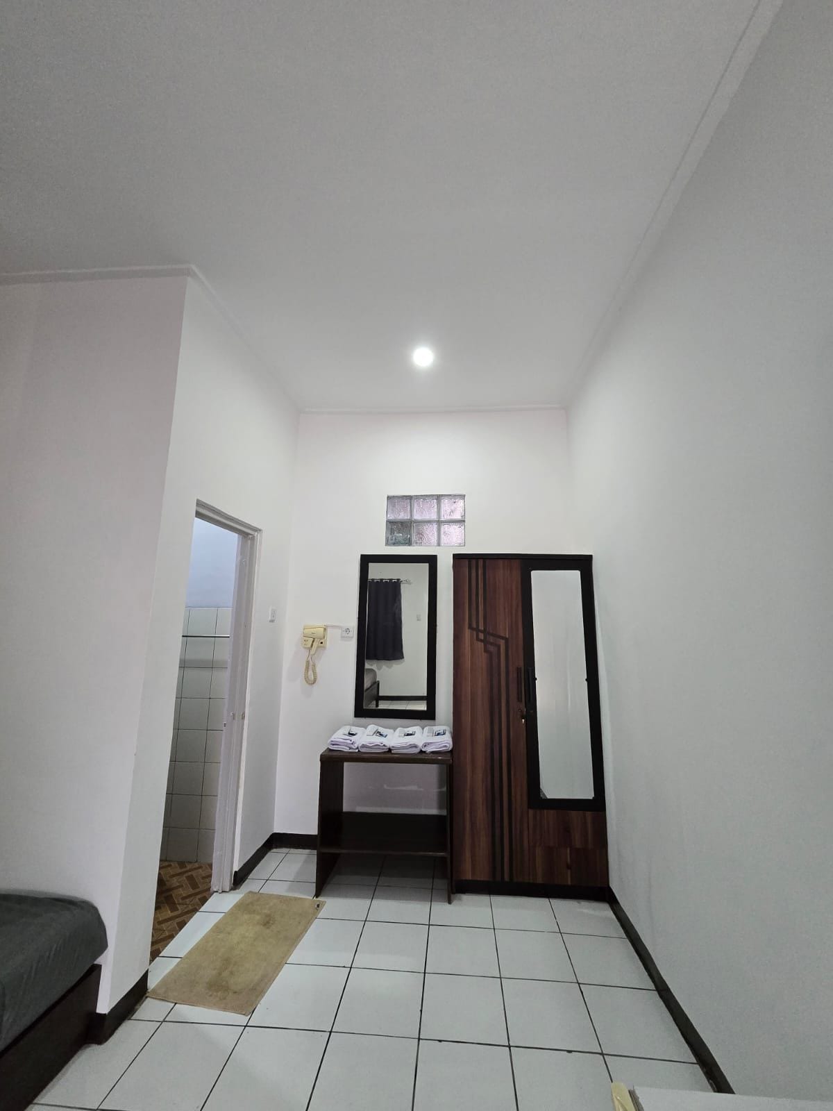 Una habitación pequeña y bien iluminada con una cama, un espejo, un armario y una mesita con toallas.