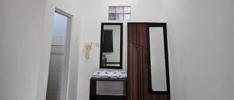 Una habitación pequeña y bien iluminada con una cama, un espejo, un armario y una mesita con toallas.