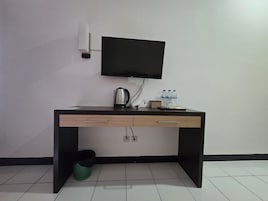 Habitación de hotel con escritorio, televisor de pantalla plana, tetera, botellas de agua y un cubo de basura.