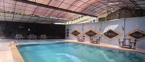 Una piscina interior de borde curvo, rodeada por un suelo con azulejos y una estructura de techo cubierta.