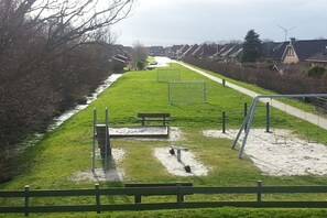 A grassy area with a bench, a playground with a swing set, and a soccer goal. - Holiday home with 2 bedrooms (Neßmersiel)