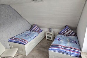 A small, compact room with two single beds, a white chair, and a nightstand with a lamp. - Holiday home with 2 bedrooms (Neßmersiel)
