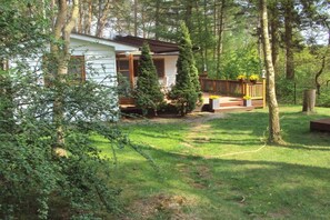 A cabin with a porch, surrounded by trees and a grassy yard. - Holiday home in Dargow with swimming pool (Dargow)