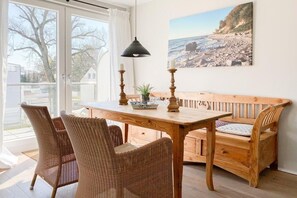 Un coin repas avec une table en bois et des chaises en osier, un banc et une suspension.