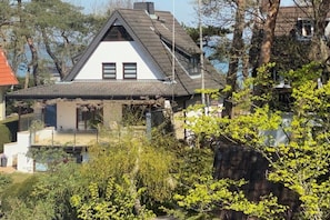 A house with a sloped roof, a balcony, and a garden with various plants. - Holiday apartment with 1 bedroom (Timmendorfer Strand)