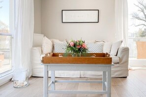 A living room with a white sofa, a wooden coffee table with a vase of flowers, and a framed picture on the wall. - Holiday apartment with 1 bedroom (Timmendorfer Strand)