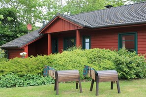 A red building with a sloped roof and a porch. There are two wooden benches in front. - Farmhouse-marsh view (Poppenbüll)