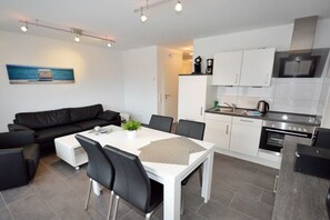 Een moderne keuken met witte kasten, een eettafel met stoelen en een zwarte leren bank.