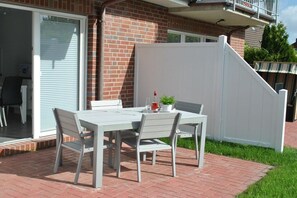 Een terras buiten met een tafel en stoelen, een wit hekwerk en een bakstenen muur.