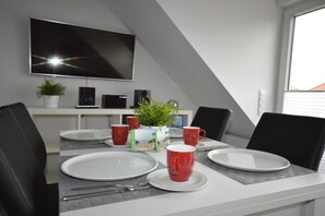 A dining area with a table set for four, a flat-screen TV mounted on the wall, and a potted plant on the table. - Holiday apartment with 1 bedroom (Norddeich)