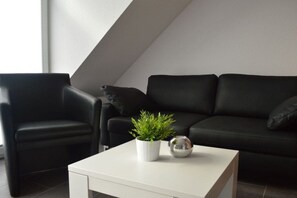 A modern living room with a black leather sofa, a white coffee table, a potted plant, and a decorative sphere. - Holiday apartment with 1 bedroom (Norddeich)