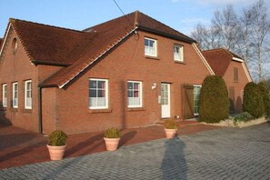A red brick house with a tiled roof, a front door, and two potted plants. - Living at the Moor 2 (Ihlow-Westersander)