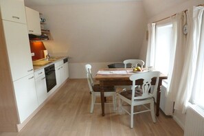 Une cuisine compacte avec des meubles blancs, un plan de travail en bois et une table à manger avec quatre chaises.