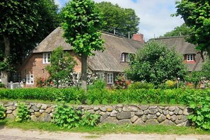 A traditional stone wall, a thatched-roof house, and a smaller building with a red window. - Holiday apartment with 2 bedrooms (Nieblum)