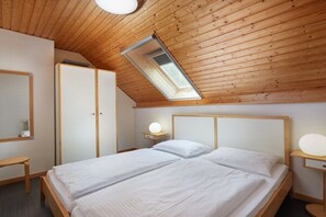 A bedroom with a sloped ceiling, a skylight, a bed with white bedding, a bedside table with a lamp, and a wardrobe. - House on the dike, harbor 3a, upper floor, 47m² (Prerow)