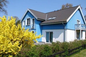 A two-story blue house with a sloped roof, a balcony on the upper floor, and a wooden fence in the foreground. - House on the dike, harbor 3a, upper floor, 47m² (Prerow)