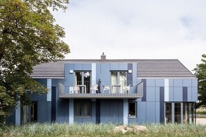 Ein modernes, zweistöckiges Gebäude mit Balkon, großen Fenstern und Flachdach.