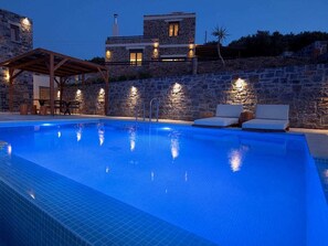 A swimming pool with lounge chairs and a stone wall. - Natural Stone House 6 (Sitia)