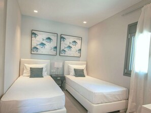 A hotel room with two beds, a nightstand, a lamp, and two wall-mounted paintings. - Natural Stone House 6 (Sitia)