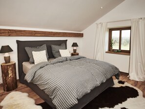 A bedroom with a large bed, two bedside tables with lamps, a window with curtains, and a wooden floor. - Holiday Home With 2 Bedrooms (Wonneberg)