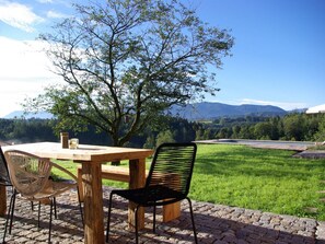 An outdoor dining area with a wooden table and chairs, a tree, and a view of mountains. - Holiday Home With 2 Bedrooms (Wonneberg)