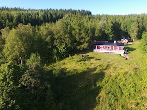 Ein rotes Haus mit weißer Veranda, umgeben von dichtem Wald.