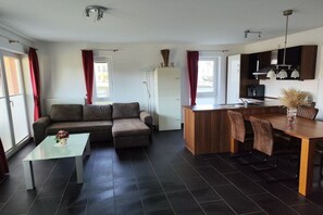 A modern living room with a sofa, a glass coffee table, and a dining area with a wooden table and chairs. - North Sea Resort Friesland (Schillig)