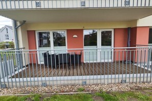 Een overdekt buitengebied met een metalen hekwerk, een zithoek met een tafel en stoelen, en een gebouw met een rood-beige gevel.