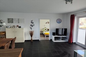 Een moderne woonkamer met een eethoek, een televisie en een bed op de achtergrond.