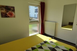 Een kamer met een bed, een raam met uitzicht op gebouwen, een radiator en een spiegel aan de muur.
