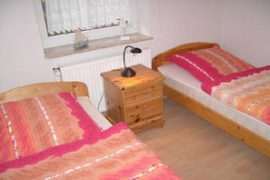 A bedroom with two beds, a nightstand, a window with curtains, and a radiator. - Holiday apartment with 2 bedrooms (Werdum)
