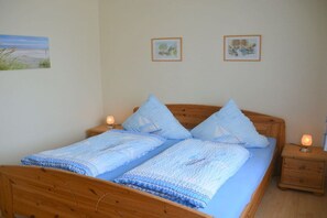 A double bed with a blue blanket and pillows, two bedside tables with lamps, and two framed pictures on the wall. - Holiday apartment with 2 bedrooms (Werdum)