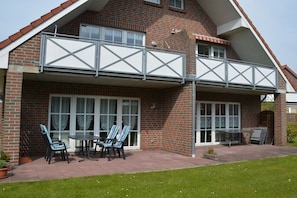 A two-story house with a balcony, a patio with chairs and a table, and a brick exterior. - Holiday apartment with 2 bedrooms (Werdum)