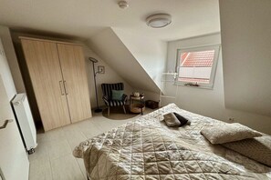 Ein Schlafzimmer mit einem Bett, einem Kleiderschrank, einem Sessel, einem kleinen Tisch und einem Fenster mit Jalousien.