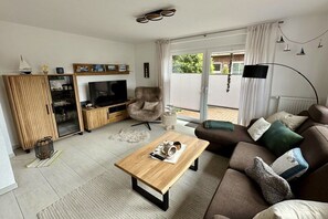 Ein Wohnzimmer mit Fernseher, einer Couch, einem Couchtisch und einer Glastür zum Außenbereich.