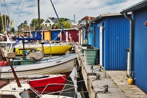 A marina with boats docked, a blue building with a door, and a red boat in the foreground. - Karstedt Court||Lübeck - Brodten (Lübeck-Brodten Travemünde)