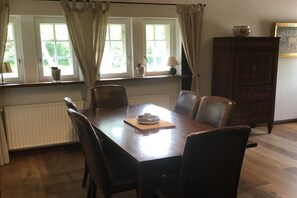 Un comedor con una mesa y sillas de madera, un radiador, un armario y ventanas con cortinas.