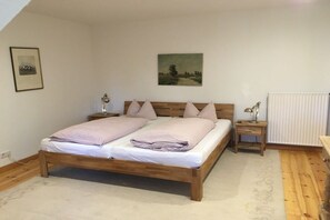 Un dormitorio con cama de madera, dos mesitas de noche, un radiador y un cuadro en la pared.